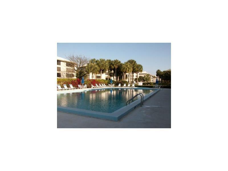 An outdoor swimming pool surrounded by lounge chairs and palm trees near a residential building — 3650 Whitehall Drive # 403, West Palm Beach FL 33401, WEST PALM BEACH, FL