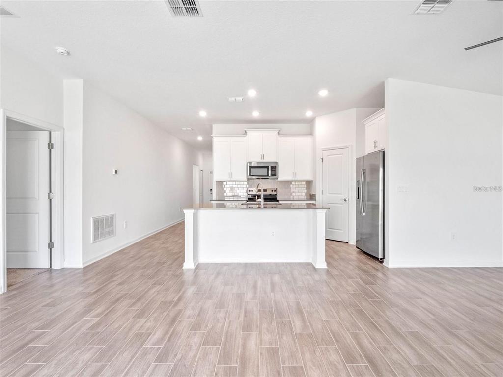 A kitchen with white cabinets, stainless steel appliances, and an island overlooks a living area — 1774 PERCH HAMMOCK LOOP, GROVELAND, FL