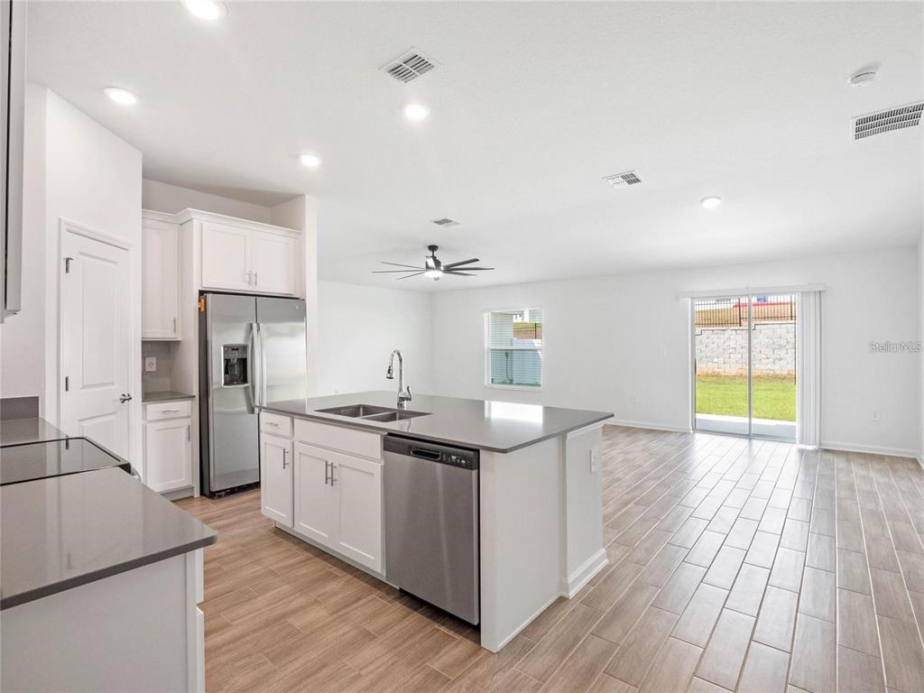 A modern kitchen with white cabinets, stainless steel appliances, and an island overlooks a living area — 1774 PERCH HAMMOCK LOOP, GROVELAND, FL