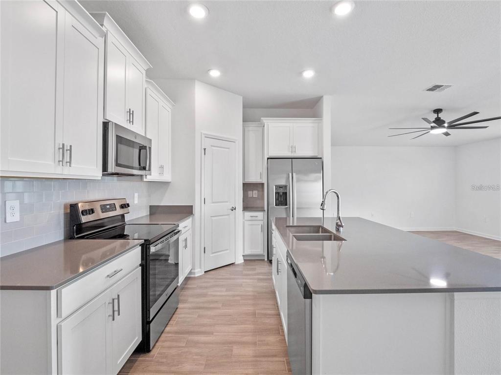 A modern kitchen features white cabinets, stainless steel appliances, and a large gray-topped island — 1774 PERCH HAMMOCK LOOP, GROVELAND, FL
