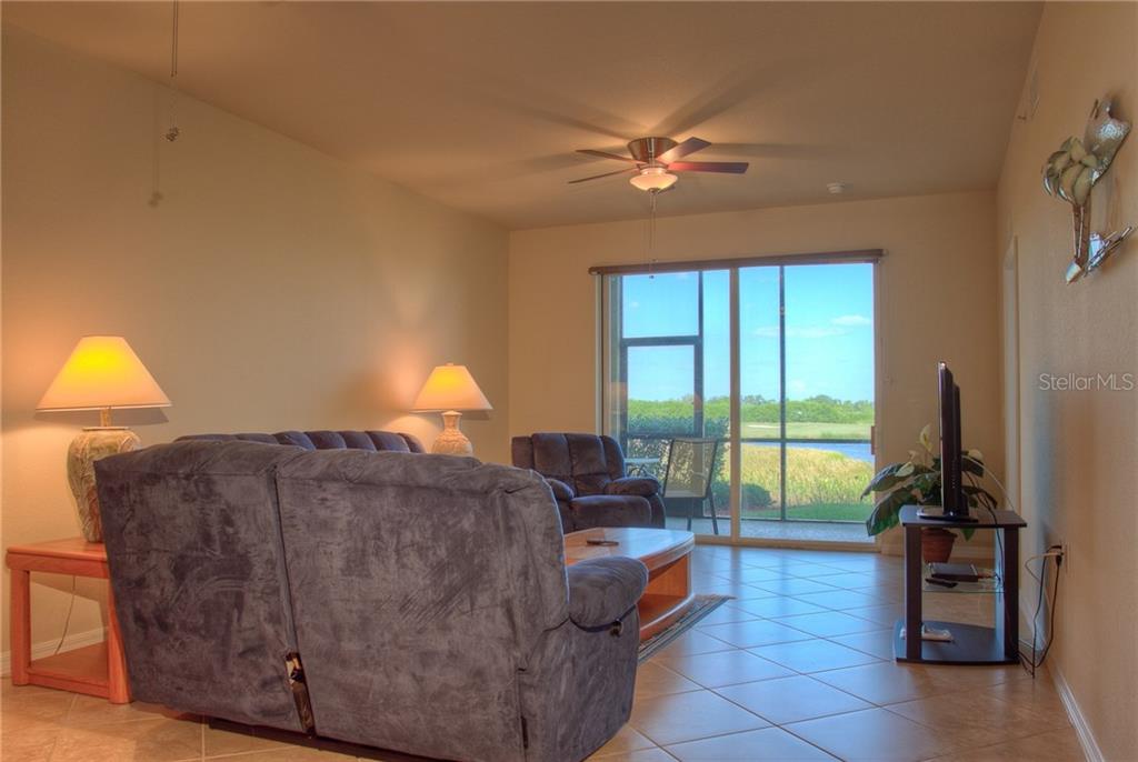 A living room features tile floors, a ceiling fan, and sliding glass doors overlooking a lake — 7705 GRAND ESTUARY TRAIL UNIT 105, BRADENTON, FL