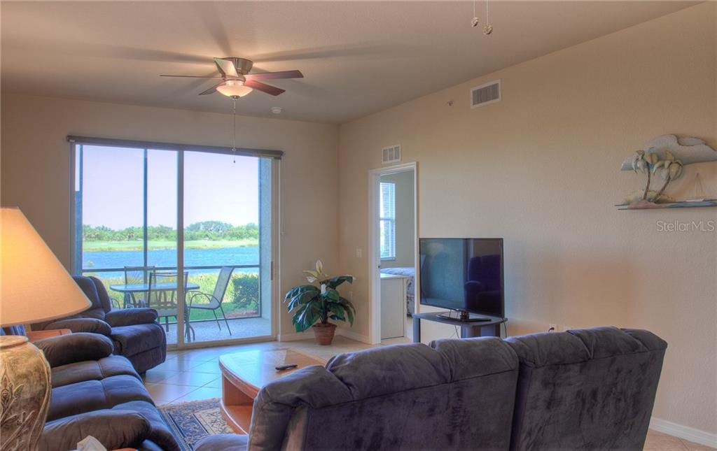 A living room with dark blue sofas, a television, and a sliding door overlooking a lake — 7705 GRAND ESTUARY TRAIL UNIT 105, BRADENTON, FL