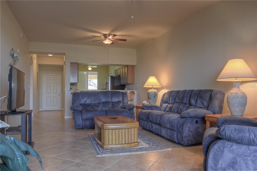 A living room features tile flooring, two blue sofas, a coffee table, and two lamps — 7705 GRAND ESTUARY TRAIL UNIT 105, BRADENTON, FL