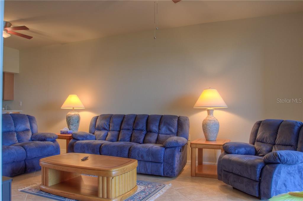 A living room features a blue sofa and two matching armchairs with two table lamps — 7705 GRAND ESTUARY TRAIL UNIT 105, BRADENTON, FL