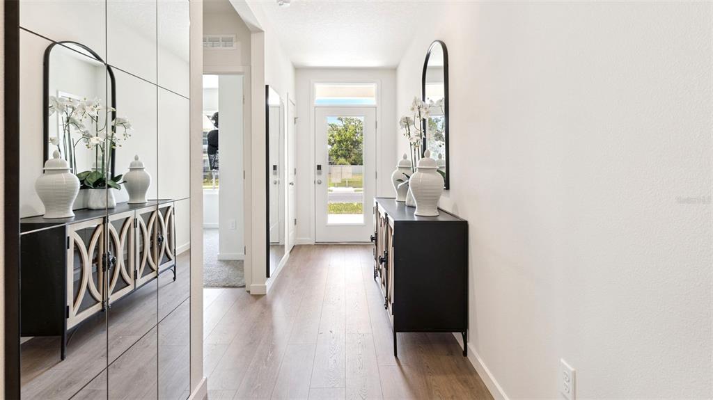 A bright entryway features light wood floors, two black console tables, and matching arched mirrors — 2891 COMMON CRANE COURT, ST CLOUD, FL