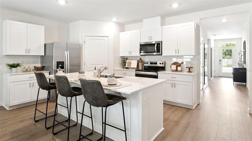 A modern kitchen features white cabinetry, stainless steel appliances, and a central island with seating — 2891 COMMON CRANE COURT, ST CLOUD, FL