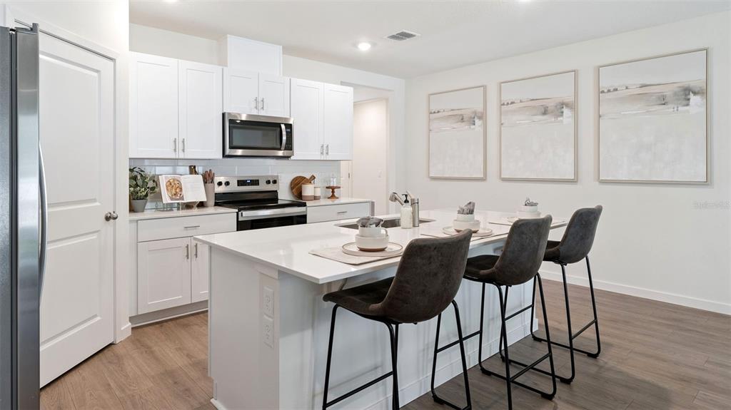A modern kitchen features white cabinetry, a central island with bar seating, and stainless appliances — 2891 COMMON CRANE COURT, ST CLOUD, FL