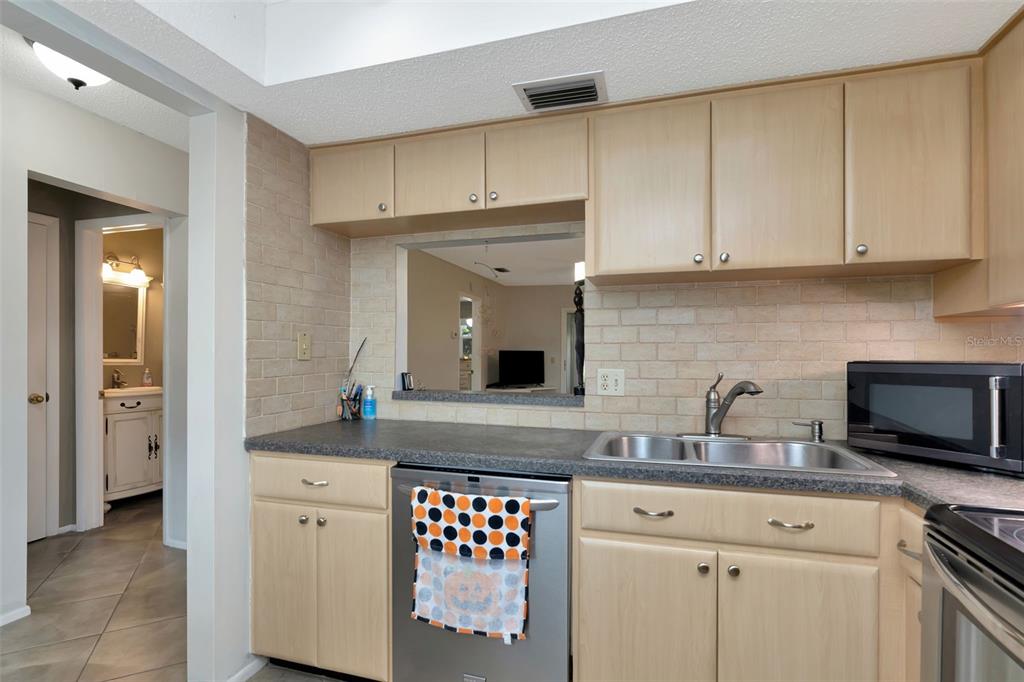 A kitchen features light wood cabinets, a brick backsplash, a double sink, and a dishwasher — 1024 DE SOTO DRIVE, DUNEDIN, FL