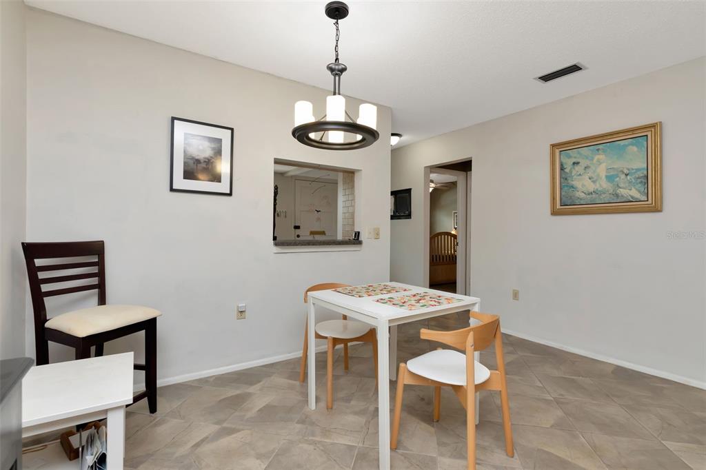 A dining area features a white table, three chairs, a chandelier, and tiled flooring — 1024 DE SOTO DRIVE, DUNEDIN, FL