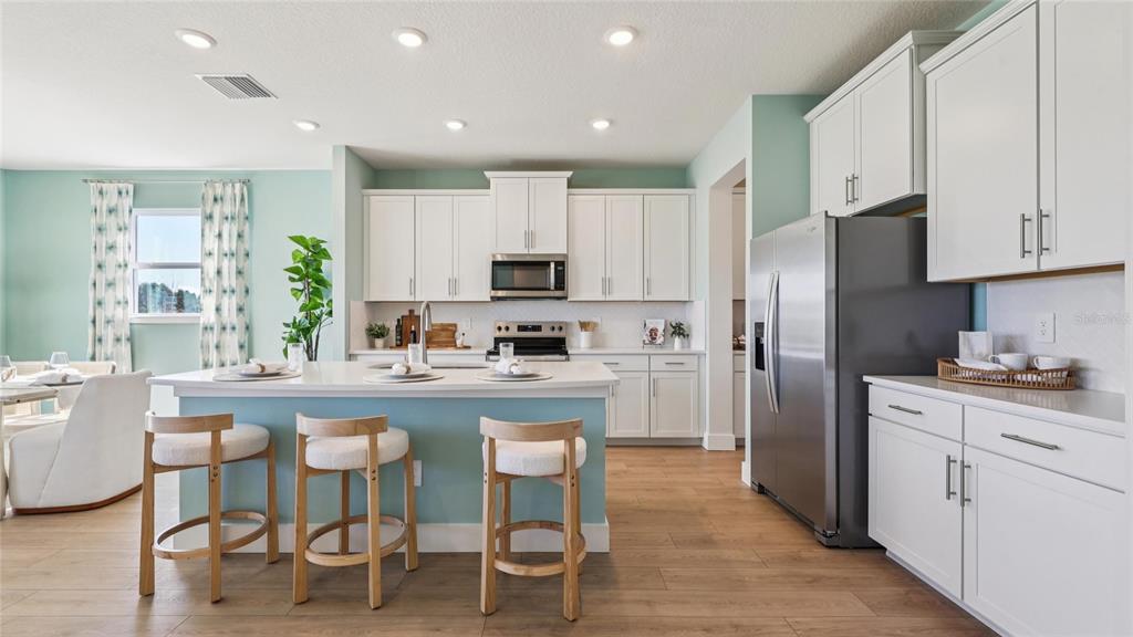 A kitchen features white cabinets, a light blue island with three stools, and stainless appliances — 4225 SW 52ND LANE ROAD, OCALA, FL