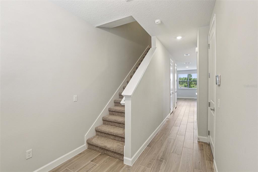 A hallway with wood-look tile flooring leads to a carpeted staircase and a windowed room — 7558 DEER VALLEY CIRCLE, TAMPA, FL