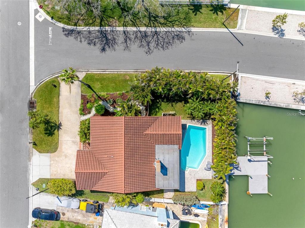 An aerial view shows a house with a tiled roof, swimming pool, and private dock — 562 JOHNS PASS AVENUE, MADEIRA BEACH, FL