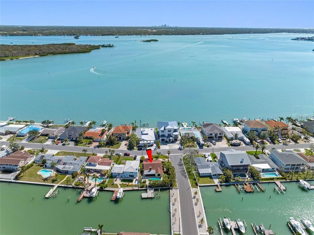 An aerial view shows a waterfront neighborhood with houses, docks, and a large bay — 562 JOHNS PASS AVENUE, MADEIRA BEACH, FL