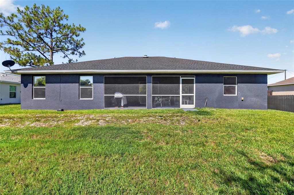 The rear exterior of a single-story house features a screened-in patio and a grassy yard — 4105 NE 20TH PLACE, CAPE CORAL, FL