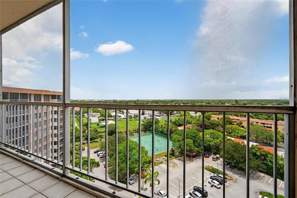 A high-angle view from a screened balcony overlooking a parking lot and a tennis court — 10777 W SAMPLE ROAD UNIT 1212, CORAL SPRINGS, FL