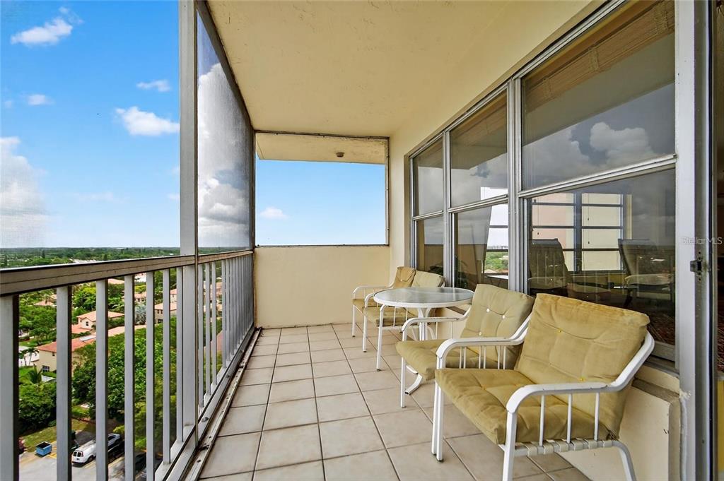 A screened-in balcony with tiled flooring, patio furniture, and a view of the surrounding area — 10777 W SAMPLE ROAD UNIT 1212, CORAL SPRINGS, FL