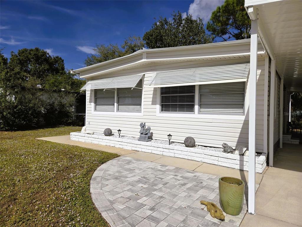 A white mobile home exterior features a stone-paved patio and a small garden bed — 3383 OAKWOOD BOULEVARD N, SARASOTA, FL