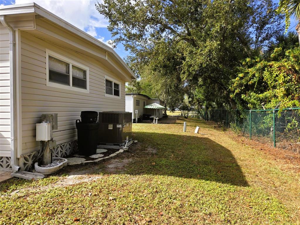The exterior side of a light-colored mobile home features an HVAC unit and a yard — 3383 OAKWOOD BOULEVARD N, SARASOTA, FL