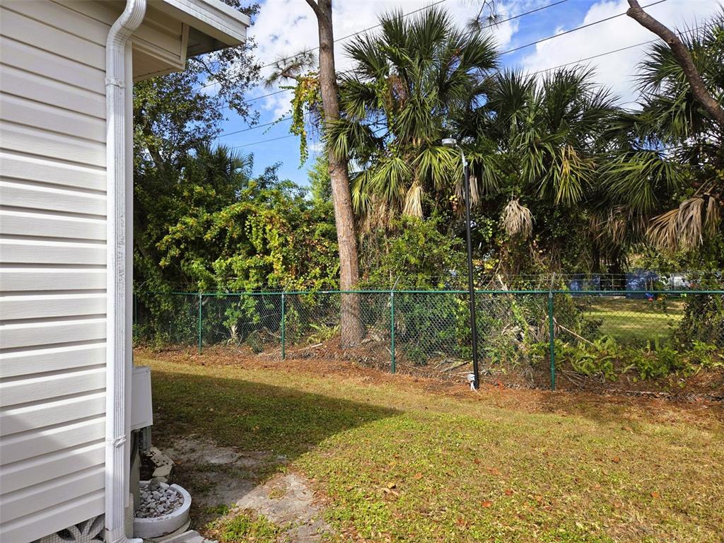 A side view of a house exterior with a chain-link fence and palm trees — 3383 OAKWOOD BOULEVARD N, SARASOTA, FL