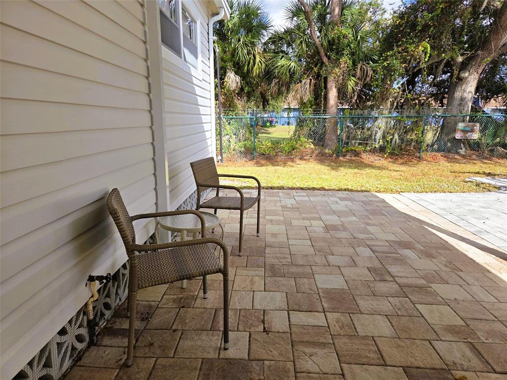A paved patio features two wicker chairs and a small table beside a house exterior — 3383 OAKWOOD BOULEVARD N, SARASOTA, FL