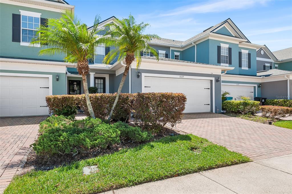 A two-story townhouse with a blue exterior, two garage doors, and two palm trees — 10077 MOORSHIRE CIRCLE, ORLANDO, FL
