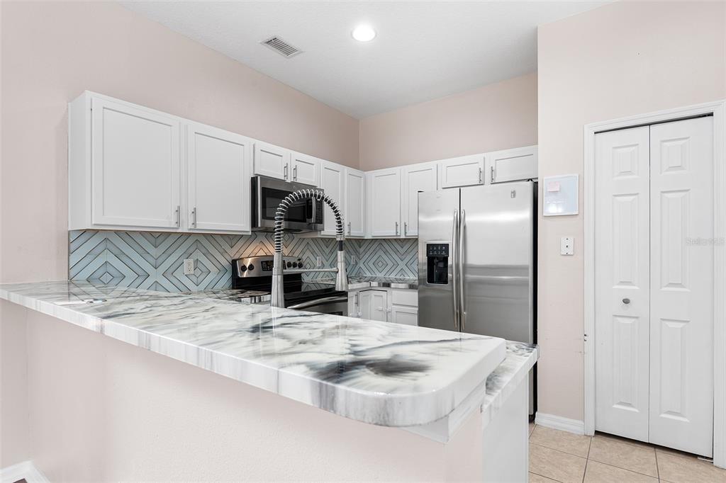 A kitchen features white cabinets, a marble-patterned countertop, stainless steel appliances, and geometric backsplash tile — 10077 MOORSHIRE CIRCLE, ORLANDO, FL
