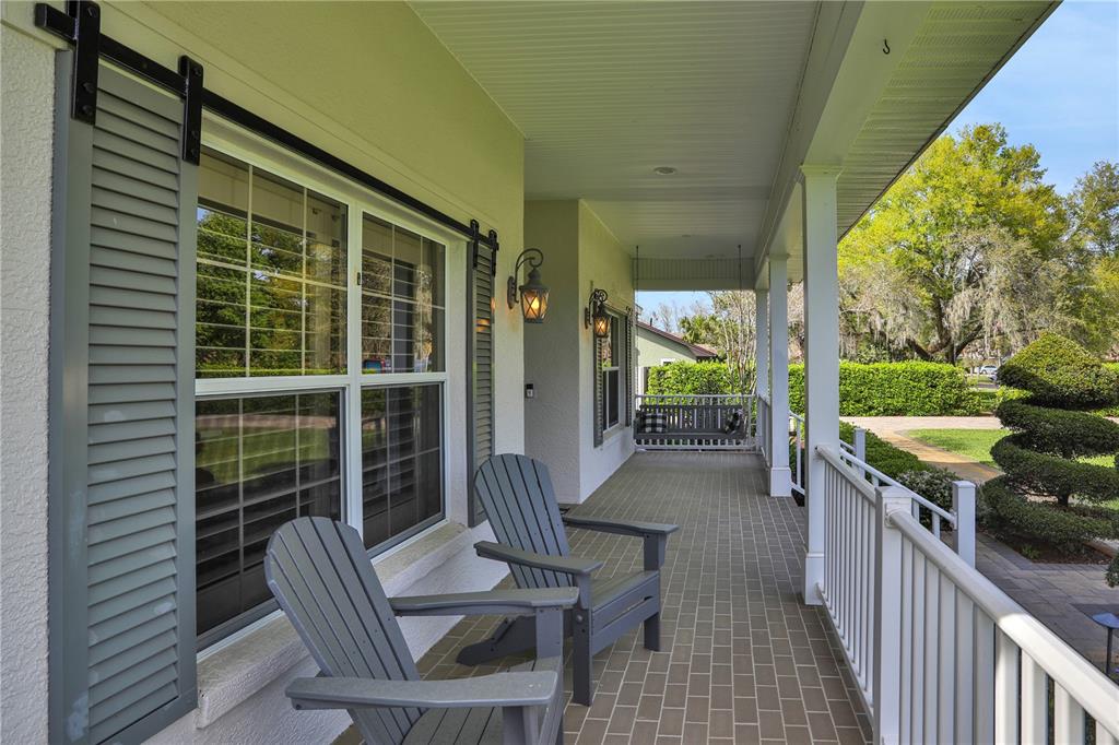 A covered front porch features gray Adirondack chairs, a hanging swing, and brick flooring — 3831 GAINES DRIVE, WINTER HAVEN, FL