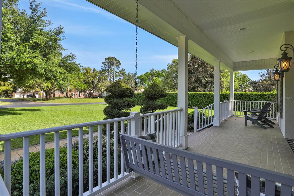 A covered front porch features a hanging swing, white railings, and a view of a lawn — 3831 GAINES DRIVE, WINTER HAVEN, FL