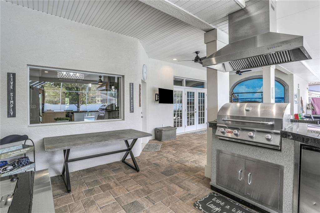 An outdoor kitchen features a stainless steel grill, a stone counter, and a dining table — 3831 GAINES DRIVE, WINTER HAVEN, FL