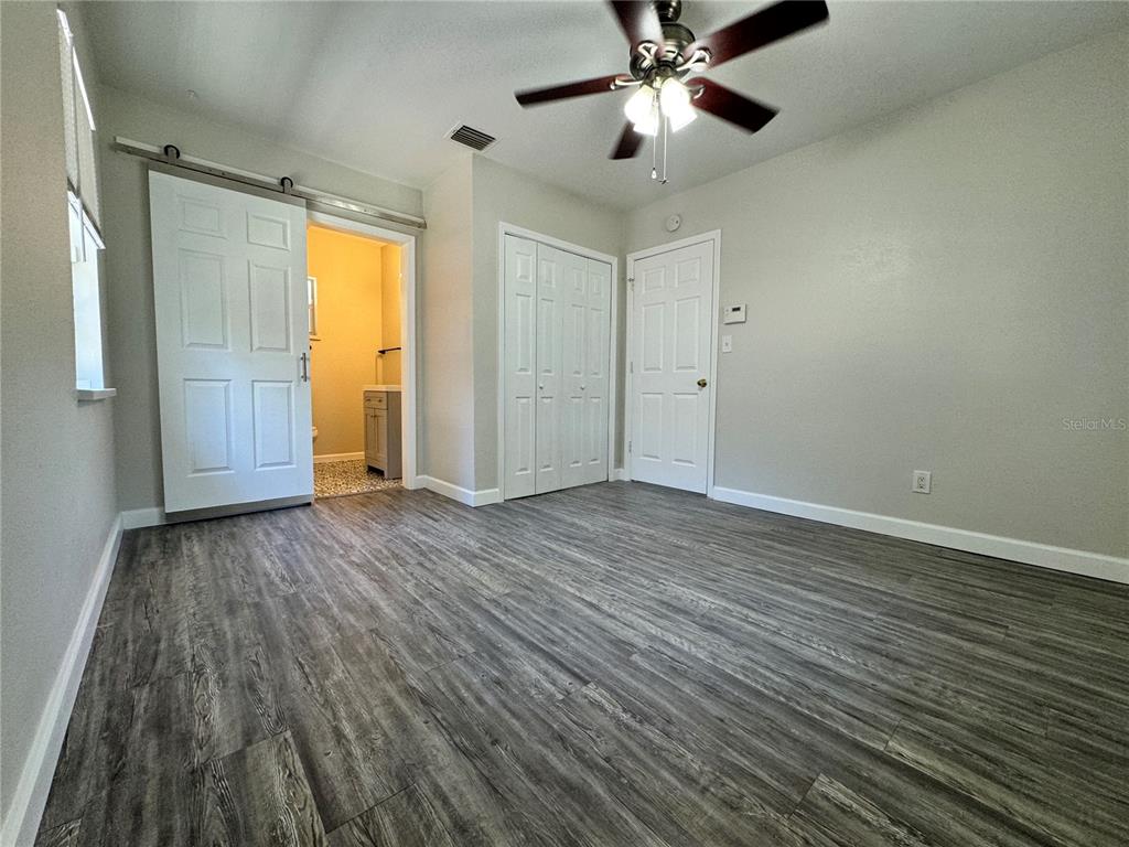 A bedroom with gray wood-look flooring, a ceiling fan, and a sliding barn door entry — 260 20TH AVENUE S, ST PETERSBURG, FL