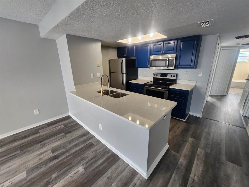 A kitchen features blue cabinets, stainless steel appliances, and a light-colored quartz island countertop — 2745 N POINCIANA BOULEVARD UNIT 63, KISSIMMEE, FL