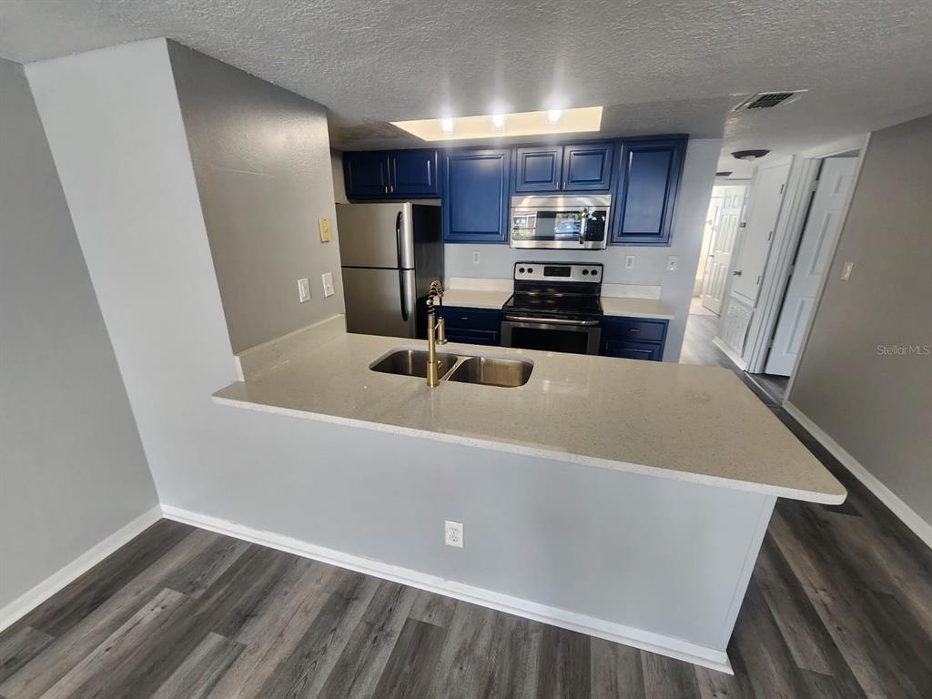 A kitchen features blue cabinets, stainless steel appliances, and a light-colored quartz countertop peninsula — 2745 N POINCIANA BOULEVARD UNIT 63, KISSIMMEE, FL