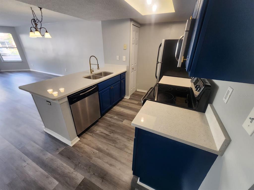 A kitchen features blue cabinets, white countertops, stainless steel appliances, and wood-look flooring — 2745 N POINCIANA BOULEVARD UNIT 63, KISSIMMEE, FL