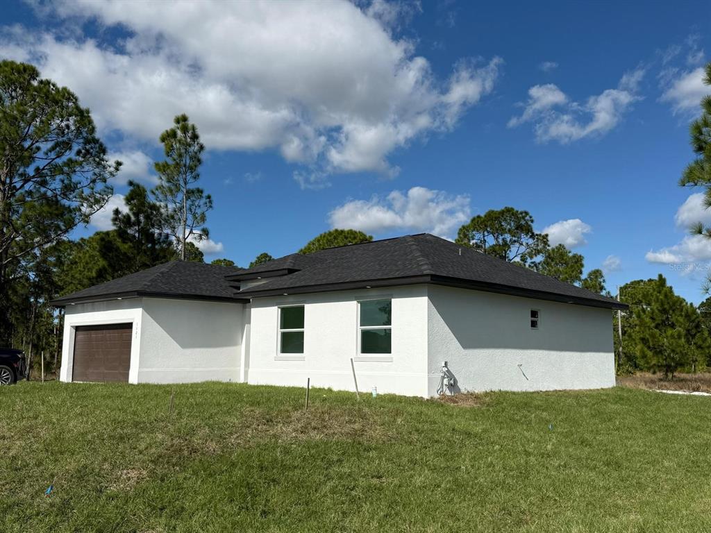 A white stucco house with a dark roof and a single-car garage under a blue sky — 1121 FLORENCE STREET E, LEHIGH ACRES, FL