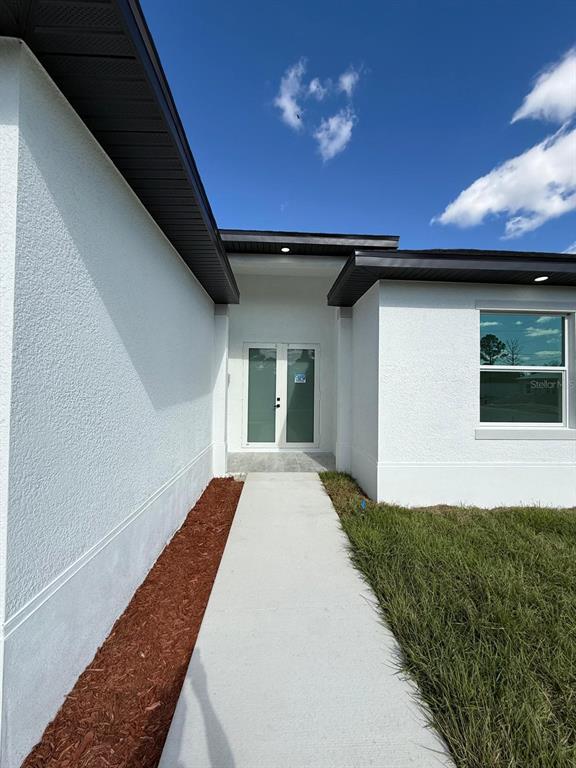 A concrete walkway leads to the double-door entrance of a white stucco house — 1121 FLORENCE STREET E, LEHIGH ACRES, FL