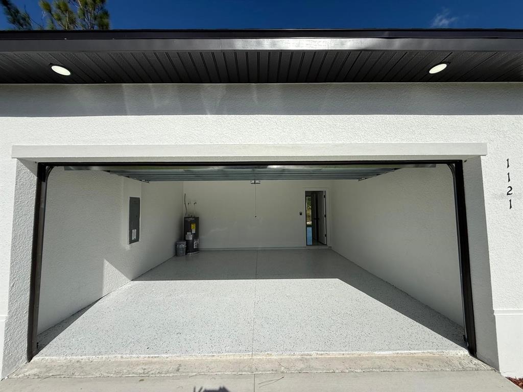 An open garage with a speckled epoxy floor, white walls, and a water heater — 1121 FLORENCE STREET E, LEHIGH ACRES, FL