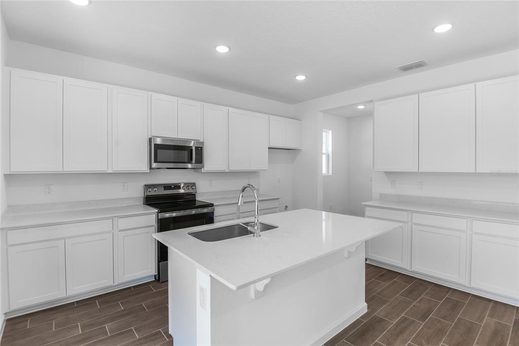 A modern kitchen features white cabinets, quartz countertops, a center island, and wood-look tile flooring — 6154 SW 64TH TERRACE, OCALA, FL