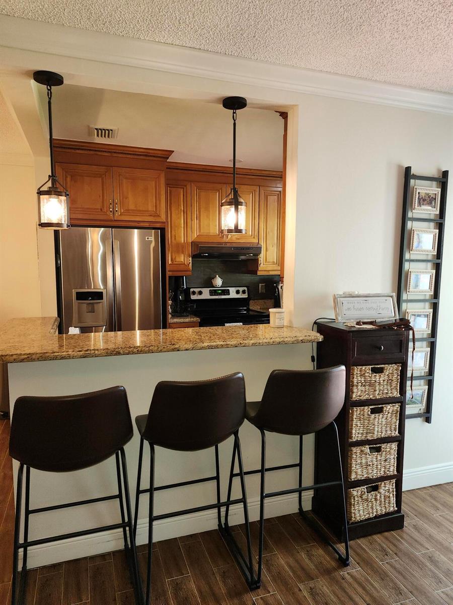 A kitchen with wood cabinets and stainless steel appliances overlooks a breakfast bar with stools — 101 Country Lane, Boynton Beach FL 33435, BOYNTON BEACH, FL