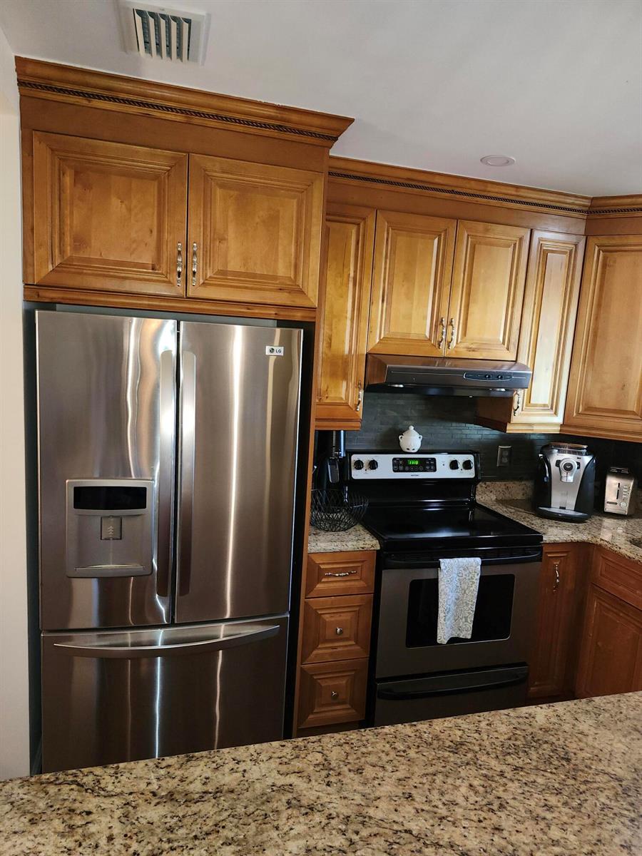 A kitchen features wood cabinets, stainless steel appliances, and granite countertops — 101 Country Lane, Boynton Beach FL 33435, BOYNTON BEACH, FL