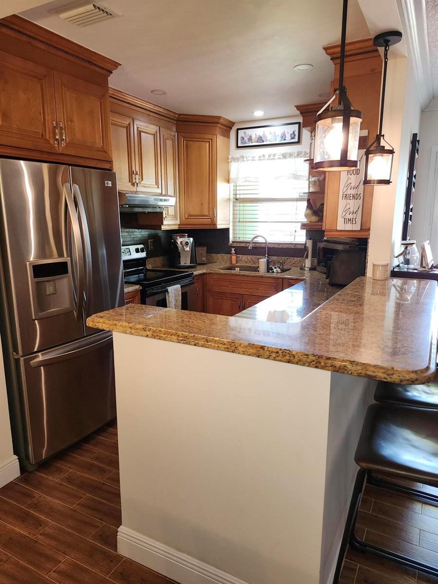 A kitchen features wood cabinets, granite countertops, stainless steel appliances, and a breakfast bar — 101 Country Lane, Boynton Beach FL 33435, BOYNTON BEACH, FL