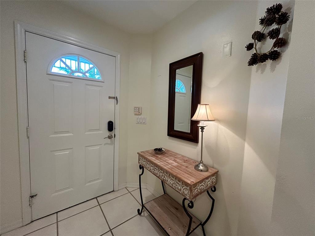 An entryway features a white front door, a console table with a lamp, and a mirror — 3605 54TH DRIVE W UNIT 203, BRADENTON, FL
