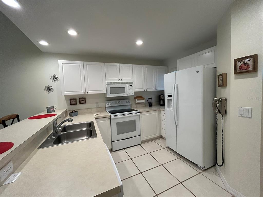 A kitchen features white cabinets, white appliances, a double sink, and light-colored tile flooring — 3605 54TH DRIVE W UNIT 203, BRADENTON, FL