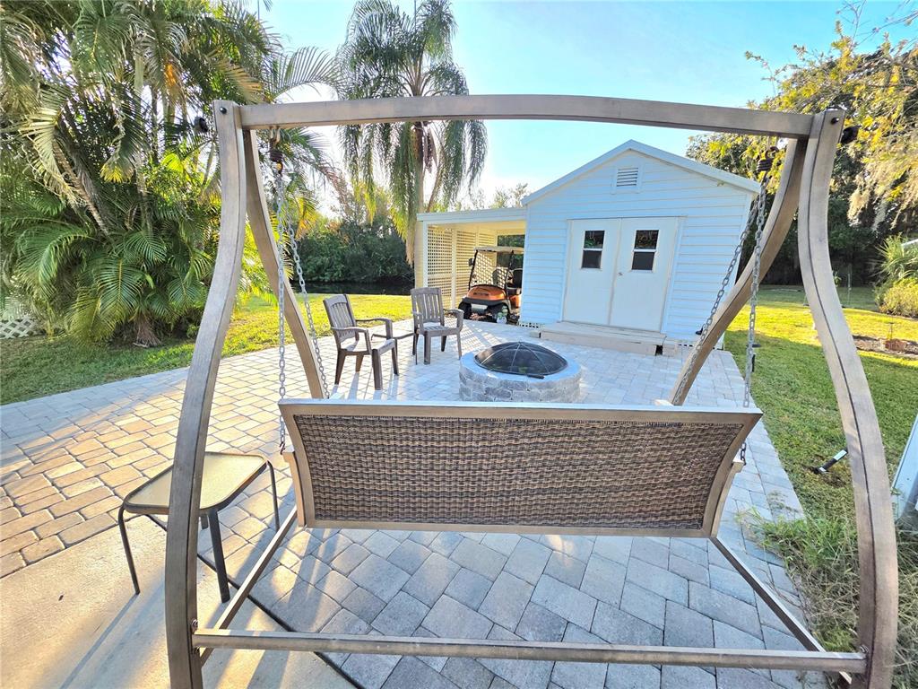A patio with a swing, fire pit, and chairs sits in front of a white shed — 26 W APPALOOSA TRAIL, RIVER RANCH, FL