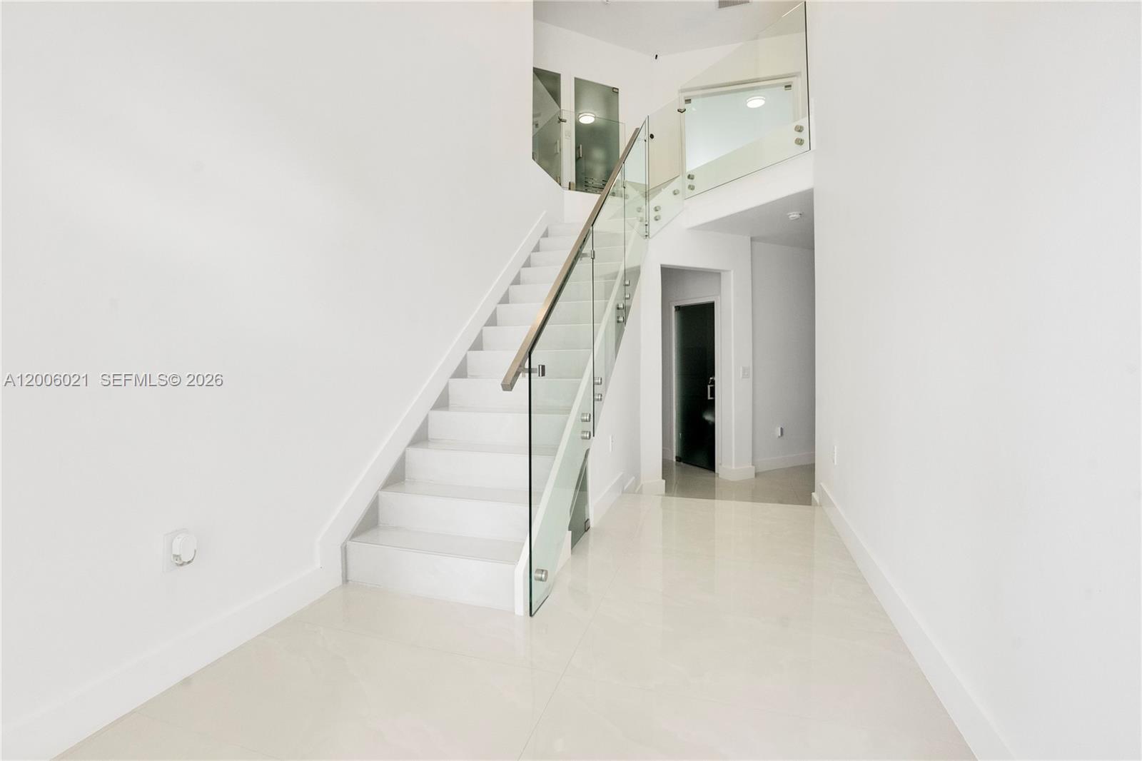 A modern white staircase features a glass railing and polished tile flooring in a hallway — 16621 SW 58th Ter, Miami FL 33193, MIAMI, FL