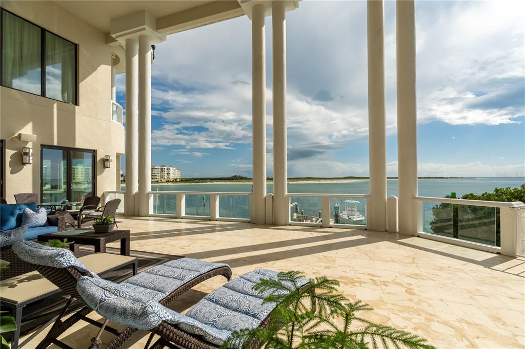 A spacious covered patio features stone flooring, white columns, and a view of the water — 774 NINA DRIVE, TIERRA VERDE, FL