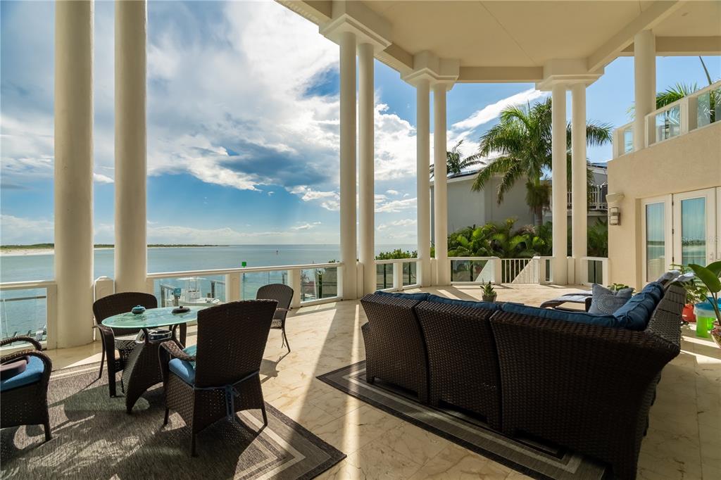 A spacious covered patio features wicker furniture, stone flooring, and expansive views of the ocean — 774 NINA DRIVE, TIERRA VERDE, FL