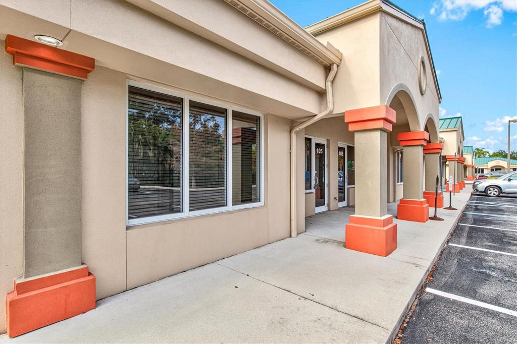 A beige commercial building exterior features orange-accented pillars and a covered walkway with glass doors — 234 N RHODES AVENUE UNIT 108, SARASOTA, FL