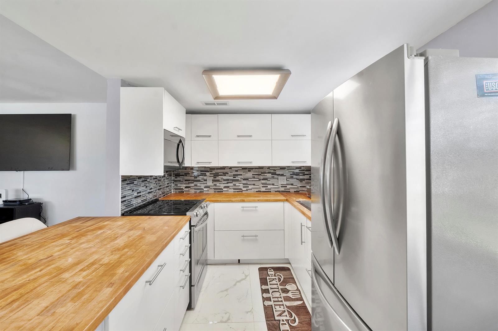 A kitchen features white cabinets, butcher block countertops, stainless steel appliances, and a tiled backsplash — 253 Prescott M, Deerfield Beach FL 33442, DEERFIELD BEACH, FL