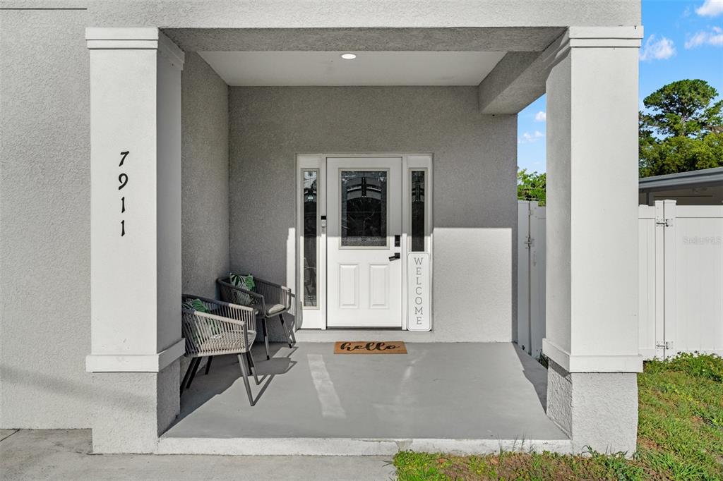 A covered front porch features a white door, two chairs, and a welcome sign — 7911 N PACKWOOD AVENUE, TAMPA, FL