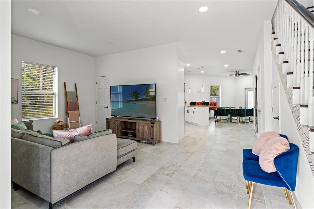 A living room with a gray sectional, television, and blue accent chair near a staircase — 7911 N PACKWOOD AVENUE, TAMPA, FL